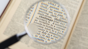 A magnifying glass highlighting the word "Challenge" in a dictionary.