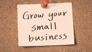 A sticky note pinned to a cork board with a red thumbtack, featuring the handwritten words 'Grow your small business' in black ink