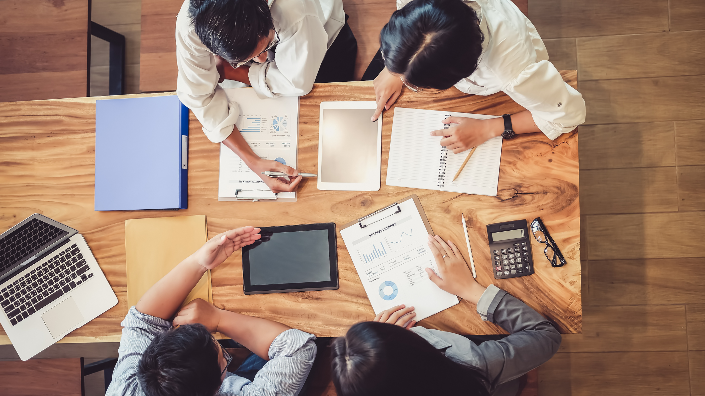 Top view of startup founders discussing reports and marketing plans around a wooden table.