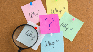 Magnifying glass over colorful sticky notes with the word 'Why?' written on them, symbolizing problem-solving and strategy review.